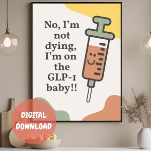 以下が含まれることがあります： 「No, I'm not dying, I'm on the GLP-1 baby!!」のテキストと漫画の注射器が描かれた、額入りのデジタルプリント。プリントは、オレンジ、黄色、緑の形をした白い背景です。デジタルダウンロードのラベルが前景にあります。
