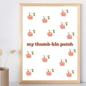 May include: A framed wall art print featuring a repeating pattern of watercolor-style peach-colored pumpkins with green stems and leaves on a white background, with the text my thumb-kin patch centered in a brown, rounded, retro-style font.