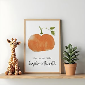May include: A rectangular wall art print in a light wood frame featuring a watercolour illustration of an orange pumpkin with green leaves and the black text "the cutest little pumpkin in the patch" centred below the pumpkin on a white background.