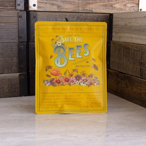 May include: Yellow pouch with a graphic of bees and flowers. The text "Save the Bees" is in a large, blue font. The pouch is labeled "Mountain Valley Seed" and "Seed Collection".