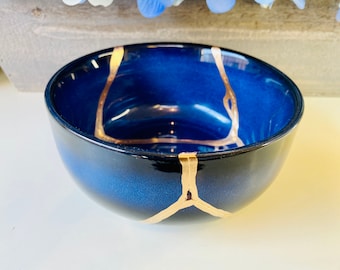 May include: A small, round bowl with a dark blue glaze and gold crackle lines. The bowl is made of ceramic and has a glossy finish.