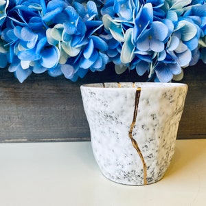 Pode incluir: Vaso de cer&acirc;mica branco com superf&iacute;cie texturizada e detalhes dourados. O vaso tem um esmalte craquelado e &eacute; decorado com finas linhas douradas.