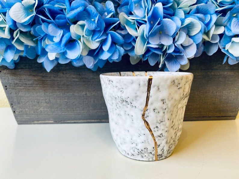 Pode incluir: Vaso de cer&acirc;mica branco com superf&iacute;cie texturizada e detalhes dourados. O vaso tem um esmalte craquelado e &eacute; decorado com finas linhas douradas.
