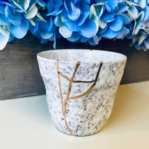 Pode incluir: Caneca de cer&acirc;mica branca com acabamento salpicado e design de rachaduras douradas. A caneca est&aacute; sobre uma superf&iacute;cie branca.