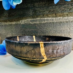 May include: A black ceramic bowl with gold accents. The bowl has a textured surface and a wide rim.