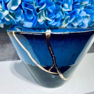 May include: A blue ceramic bowl with gold crackle glaze. The bowl is slightly angled and has a wide rim.