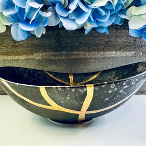 May include: A black oval bowl with gold accents. The bowl has a speckled finish and is decorated with gold lines.