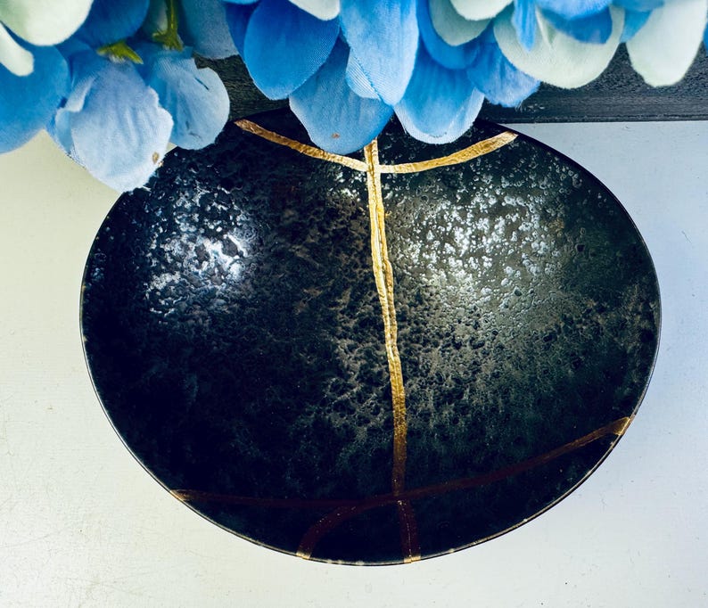 May include: A black ceramic bowl with gold accents. The bowl has a textured surface and a slightly rounded shape.