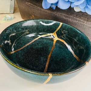 Könnte beinhalten: Eine dunkelblaue Keramikschüssel mit goldenen Rissen. Die Schüssel ist eine traditionelle japanische Kintsugi-Schüssel.