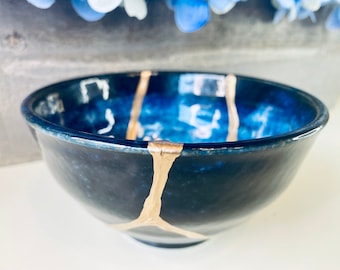 May include: A dark blue ceramic bowl with gold accents. The bowl has a crackled glaze and is decorated with gold lines.