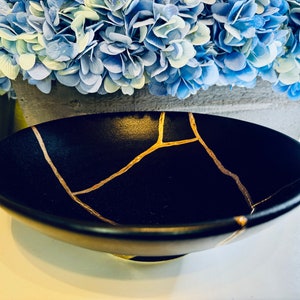 May include: A black ceramic bowl with gold crackle glaze. The bowl is empty and sitting on a white surface.