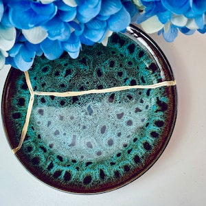 May include: A dark green and brown ceramic plate with a gold crackle design. The plate has a unique, rustic look.