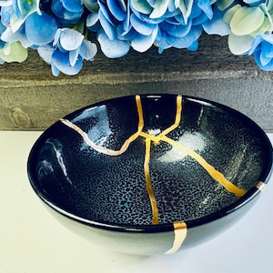 May include: A black ceramic bowl with gold cracks. The bowl has a speckled texture and is perfect for serving snacks or desserts.