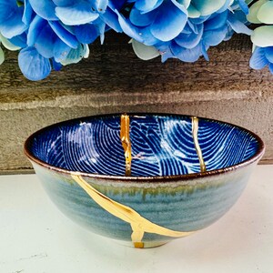 May include: A blue and gold ceramic bowl with a wavy pattern. The bowl has a crack with gold paint running through it.