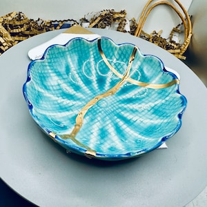 Könnte beinhalten: Eine blaue und weiße Keramikschale mit goldenem Design. Die Schale hat einen gewellten Rand und eine strukturierte Oberfläche.