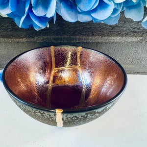 May include: A dark brown ceramic bowl with gold accents. The bowl has a speckled glaze and a rounded shape.