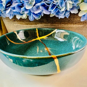 May include: A teal blue ceramic bowl with gold crackle lines. The bowl is round and has a smooth, glossy finish.