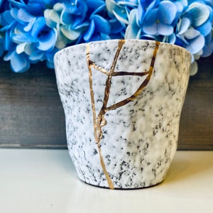 Pode incluir: Uma caneca de cer&acirc;mica branca com um esmalte craquelado e detalhes dourados. A caneca tem um aspecto envelhecido e &eacute; perfeita para adicionar um toque de charme r&uacute;stico &agrave; decora&ccedil;&atilde;o da sua casa.