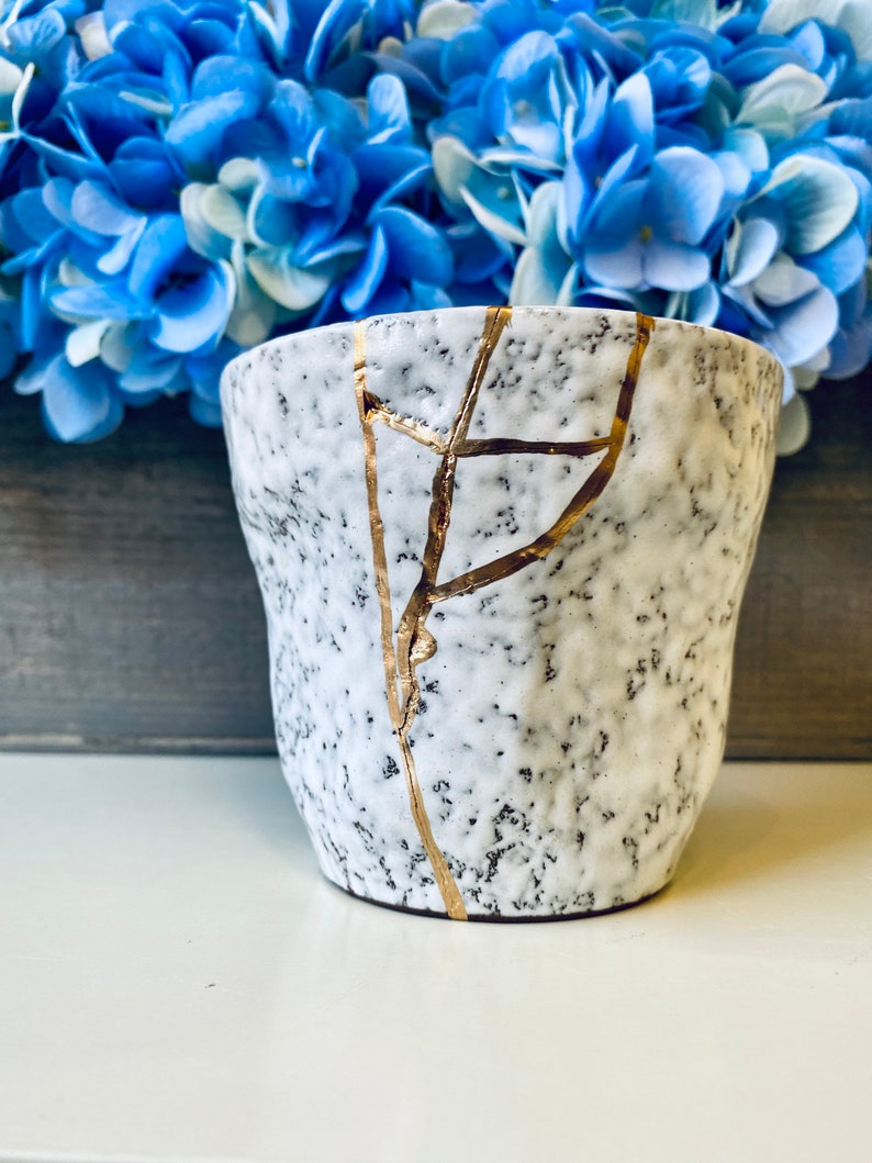 Pode incluir: Uma caneca de cer&acirc;mica branca com um esmalte craquelado e detalhes dourados. A caneca tem um aspecto envelhecido e &eacute; perfeita para adicionar um toque de charme r&uacute;stico &agrave; decora&ccedil;&atilde;o da sua casa.