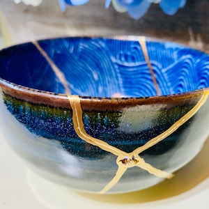 Puede incluir: Un cuenco de cerámica azul y negro con grietas doradas. El cuenco tiene un diseño texturizado y ondulado.