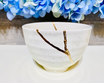 May include: White ceramic bowl with a gold crackle design. The bowl has a textured surface and a rounded shape.