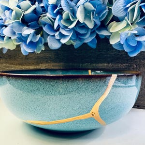 May include: A teal blue ceramic bowl with a crackled glaze and gold accents. The bowl is slightly chipped on the rim.