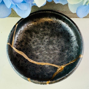May include: A black ceramic bowl with gold crackle glaze. The bowl has a textured surface and a wide rim.