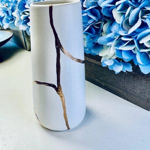 May include: White ceramic vase with gold crackle design. The vase is tall and slender with a rounded bottom.
