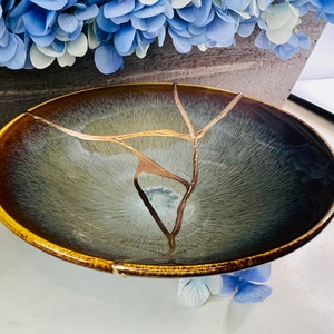 May include: A large, round, blue and brown ceramic bowl with a gold crackle glaze. The bowl has a wide rim and a deep interior.