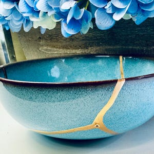 May include: A turquoise blue ceramic bowl with a crackled glaze and gold accents. The bowl has a dark brown rim.