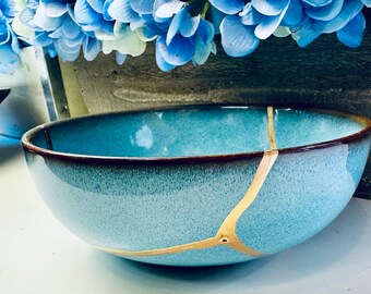 May include: A turquoise blue ceramic bowl with a crackled glaze and gold accents. The bowl has a dark brown rim.