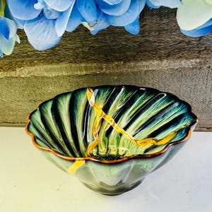 May include: A green and gold ceramic bowl with a scalloped rim. The bowl has a textured, wavy design and a gold rim.