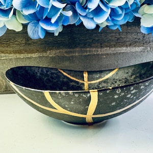 May include: A black oval bowl with gold accents. The bowl has a speckled finish and is ideal for serving snacks or holding small items.