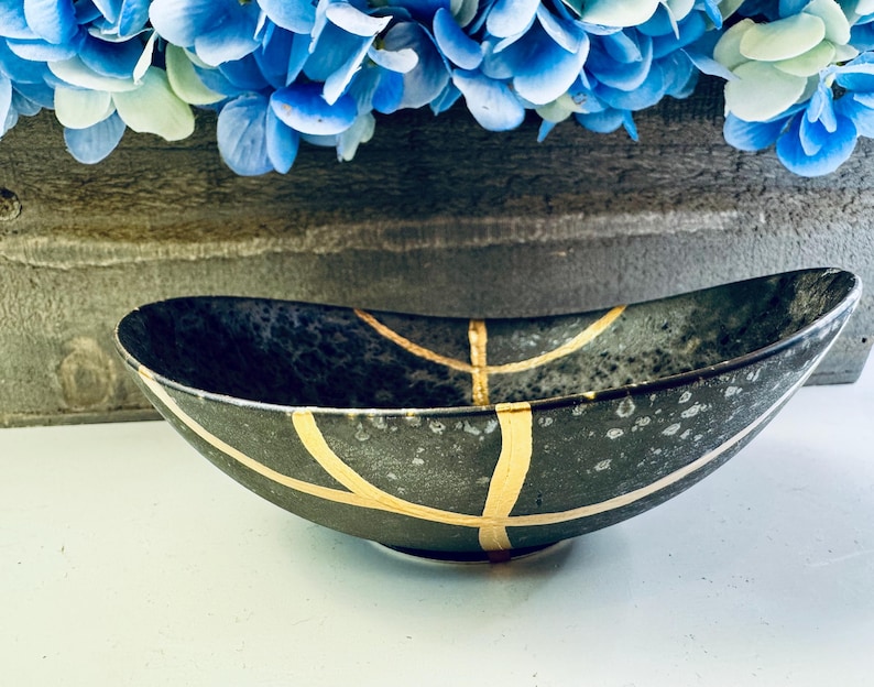 May include: A black oval bowl with gold accents. The bowl has a speckled finish and is ideal for serving snacks or holding small items.