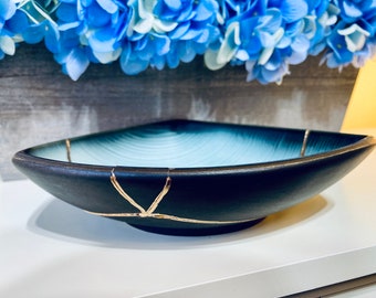 May include: A square, blue and black ceramic bowl with gold crackle lines. The bowl is slightly angled and has a light blue interior.