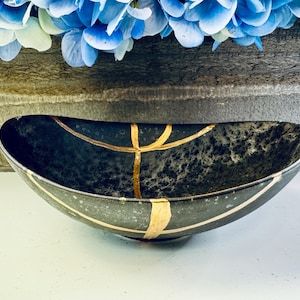 May include: A black ceramic bowl with gold accents. The bowl is oval shaped and has a speckled finish.