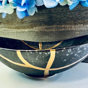 May include: A black oval bowl with gold accents. The bowl has a speckled finish and a wide, shallow shape.