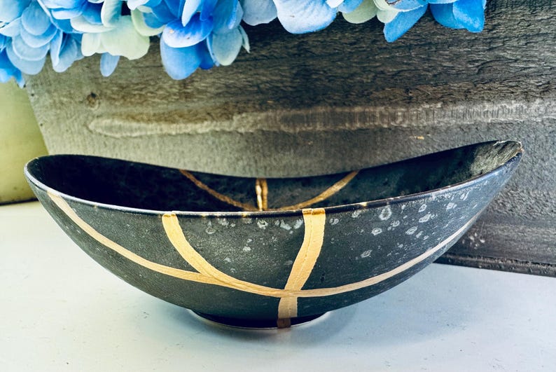 May include: A black oval bowl with gold accents. The bowl has a speckled finish and a wide, shallow shape.