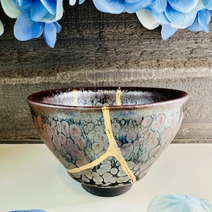 May include: A dark gray ceramic bowl with a crackled glaze and gold accents. The bowl has a unique design with a pattern of small, white dots.