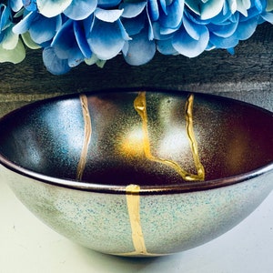 May include: A dark brown ceramic bowl with a speckled glaze and gold accents. The bowl has a wide rim and a rounded bottom.