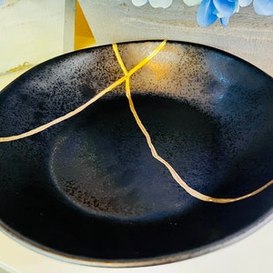 May include: A black ceramic bowl with gold crackle lines. The bowl is empty and has a textured surface.