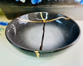 May include: A small, round, gray ceramic bowl with a crackled glaze and gold accents. The bowl has a white interior and a subtle speckled pattern.