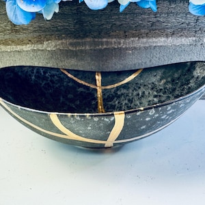 May include: A black oval bowl with gold accents. The bowl has a speckled, textured surface.