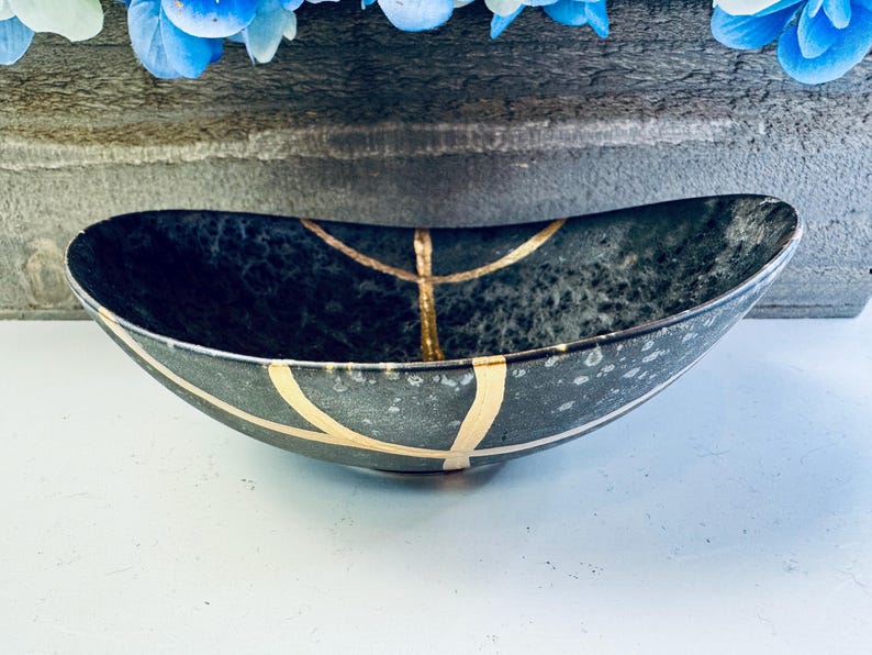 May include: A black oval bowl with gold accents. The bowl has a speckled, textured surface.
