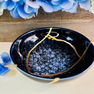 May include: A small, dark blue ceramic bowl with gold crackle lines. The bowl has a textured, speckled surface.