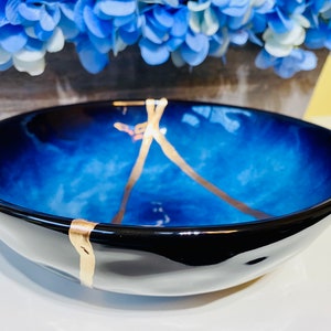 May include: A blue and black ceramic bowl with gold accents. The bowl has a wavy, organic shape and a glossy finish.
