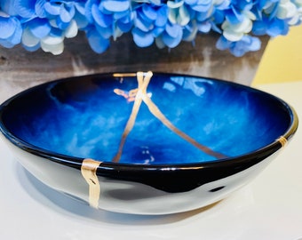 May include: A blue and black ceramic bowl with gold accents. The bowl has a wavy, organic shape and a glossy finish.