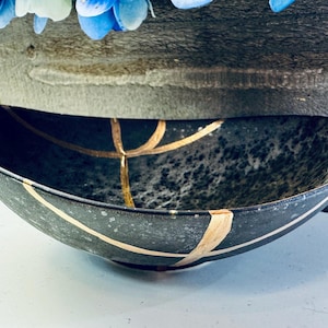 May include: A black oval ceramic bowl with gold accents. The bowl has a speckled finish and is decorated with gold lines.