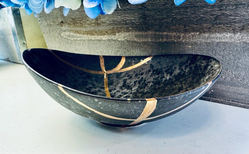 May include: A black oval ceramic bowl with gold accents. The bowl has a speckled finish and is decorated with gold lines.