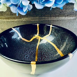 May include: A black ceramic bowl with gold cracks. The bowl has a speckled, textured surface.